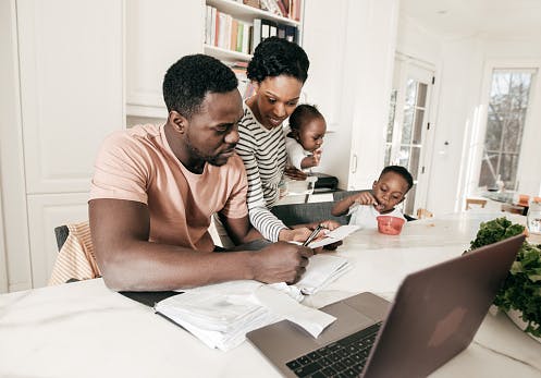 Uma família negra, com duas crianças, sentado à mesa de jantar com um computador e verificando as finanças.